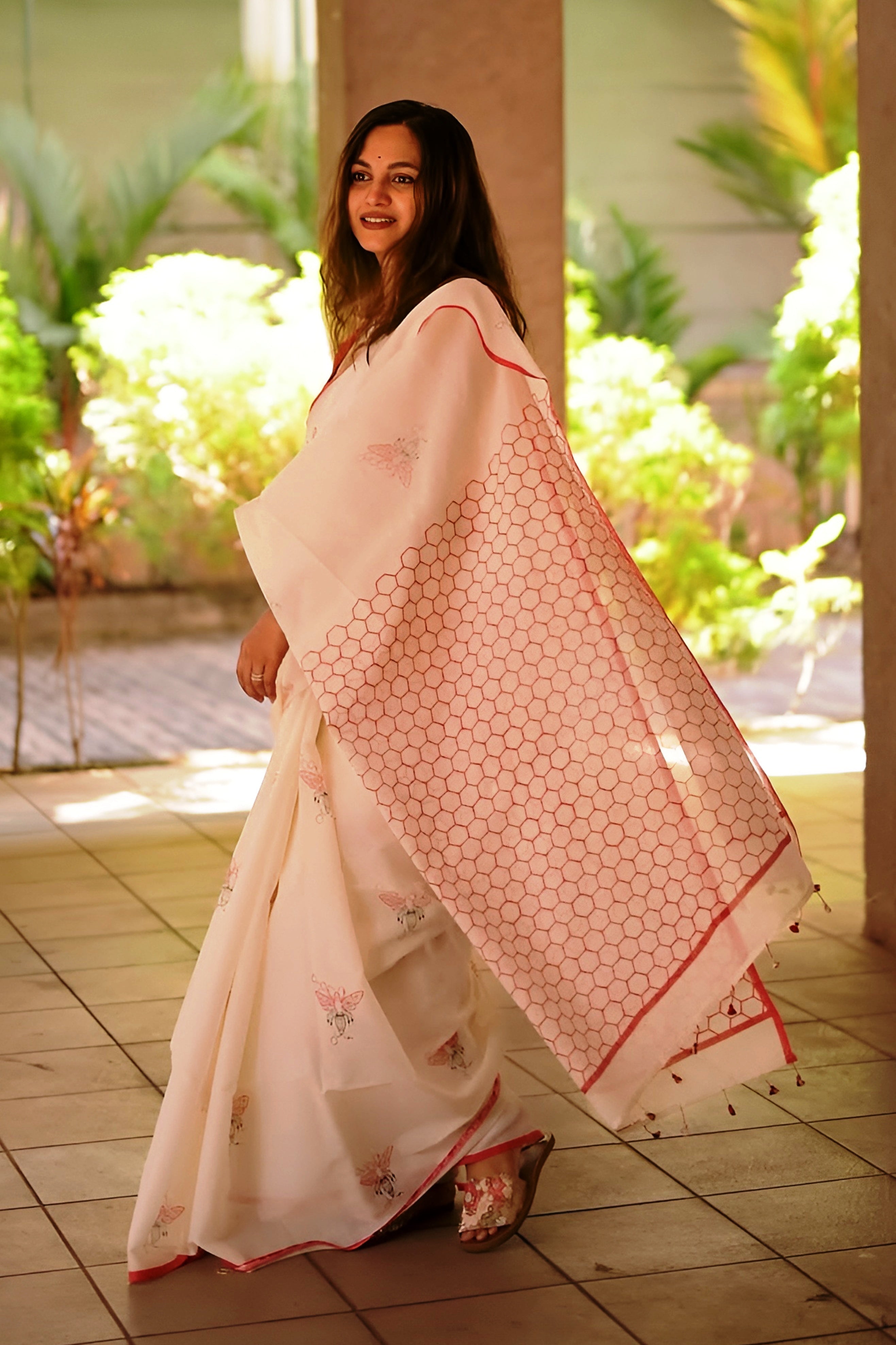 Woman holding a pink saree with a geometric pattern in an outdoor setting