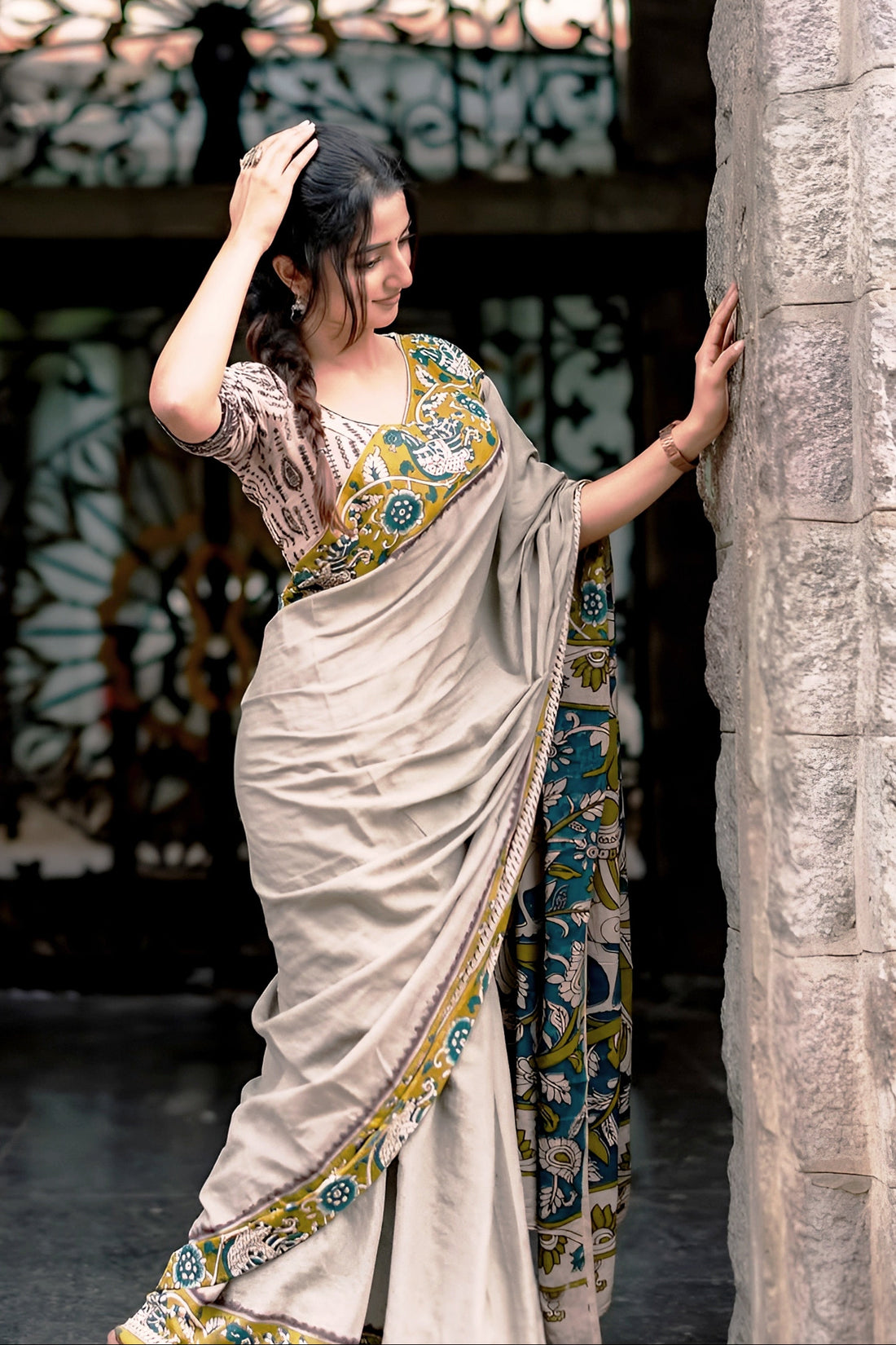 Woman in a traditional saree standing against a stone wall with decorative background