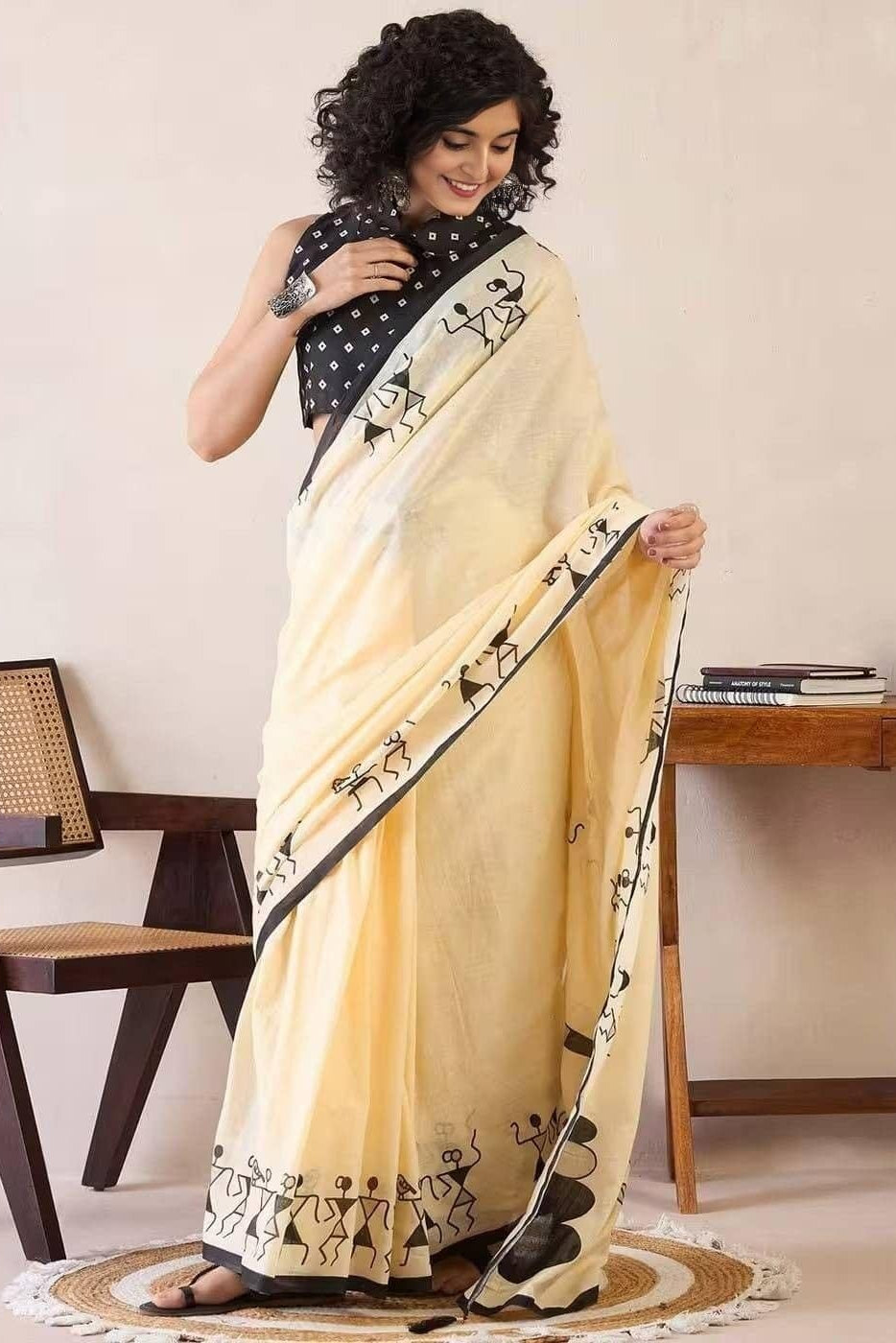 Woman wearing a beige saree with black patterns in a room setting.