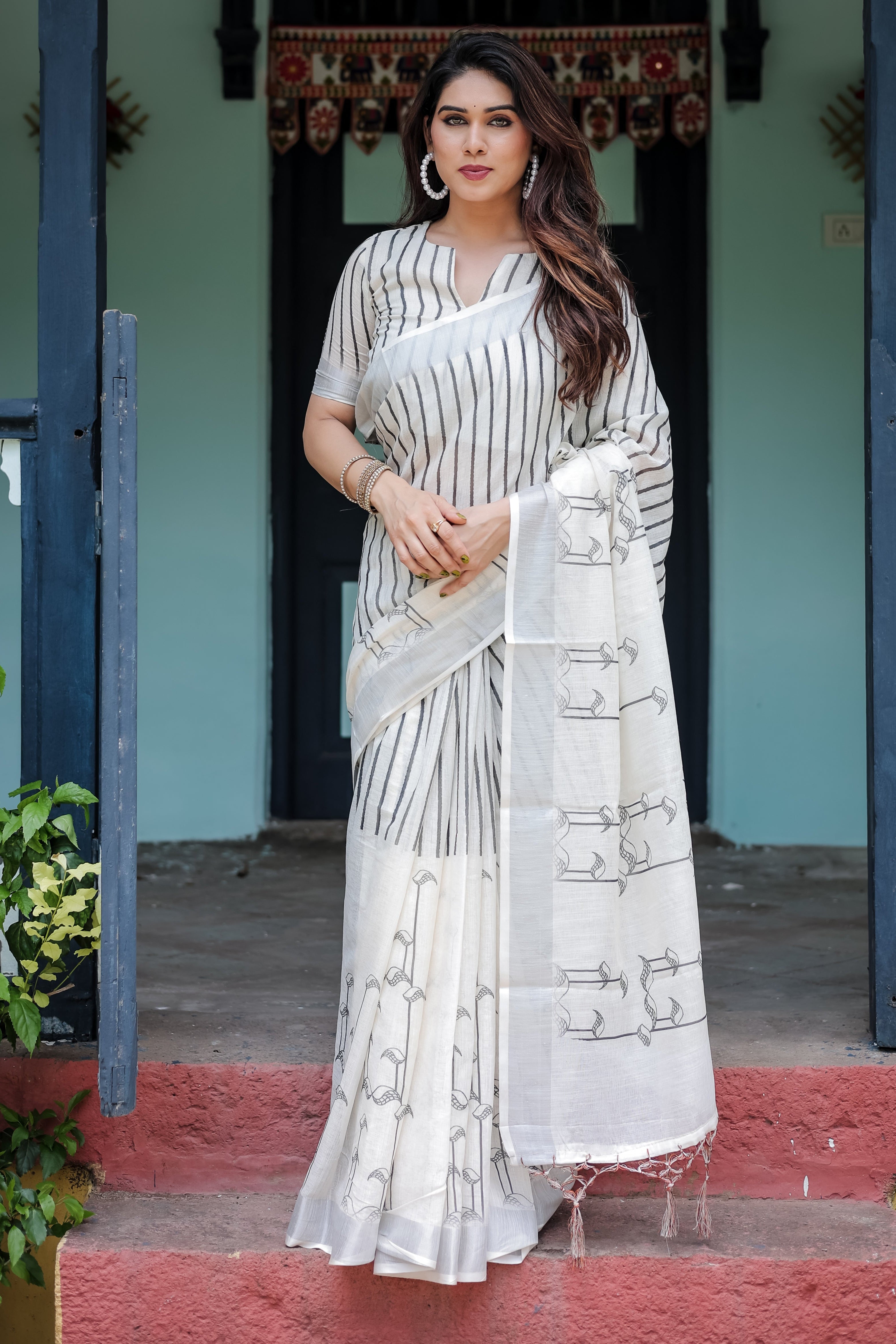 Woman in a white saree with black patterns standing in front of a traditional building.