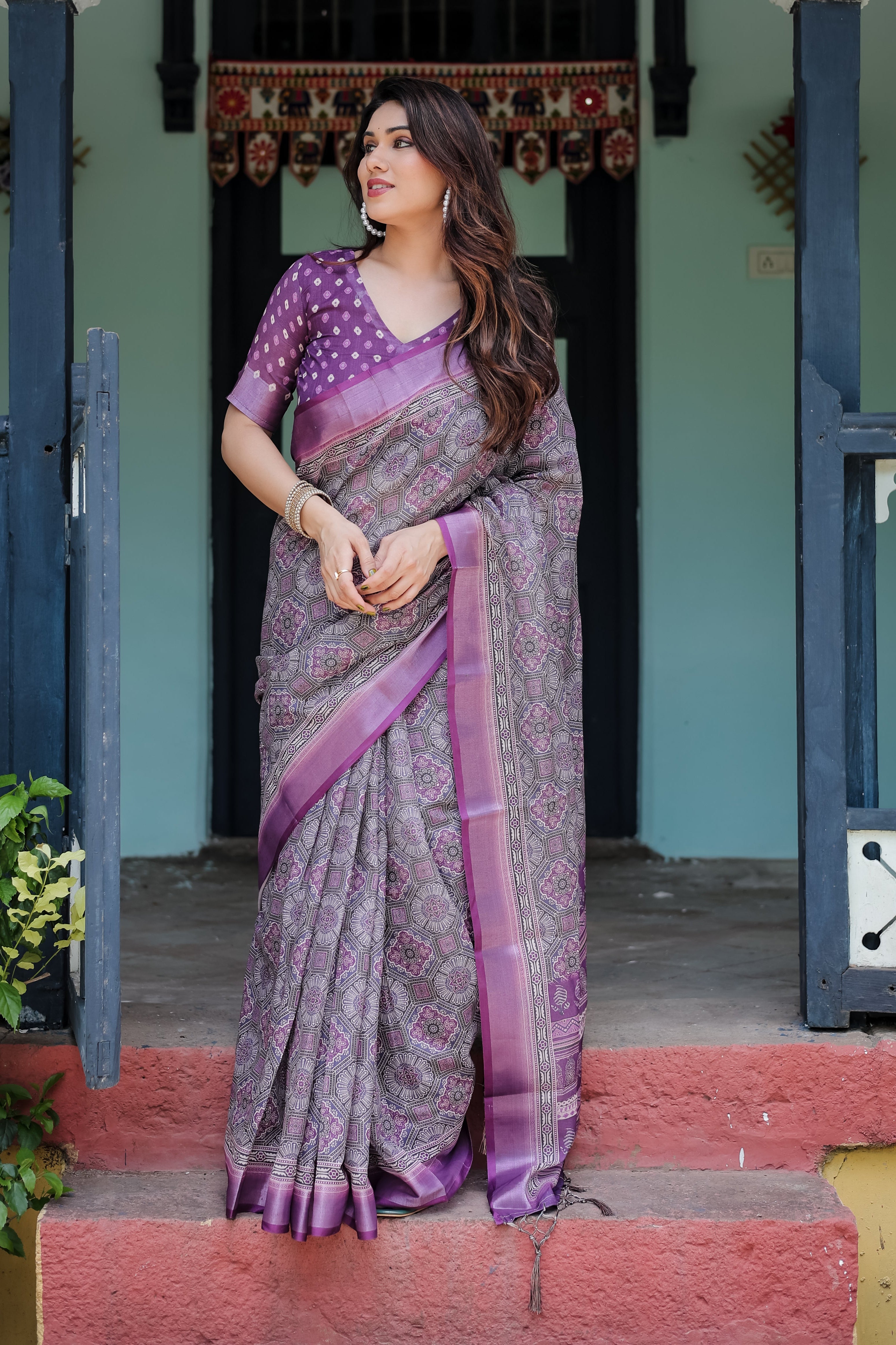 Woman in a traditional saree standing on steps with a decorative background