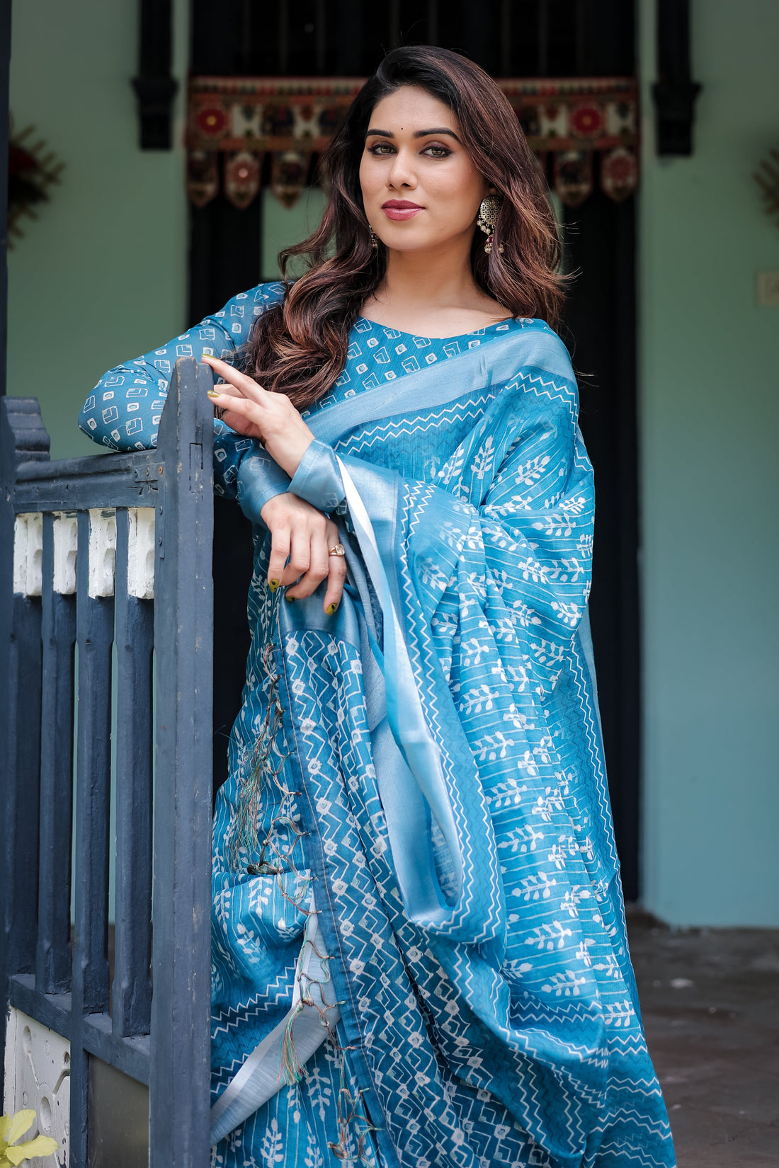 Woman in a blue saree standing against a light green wall.