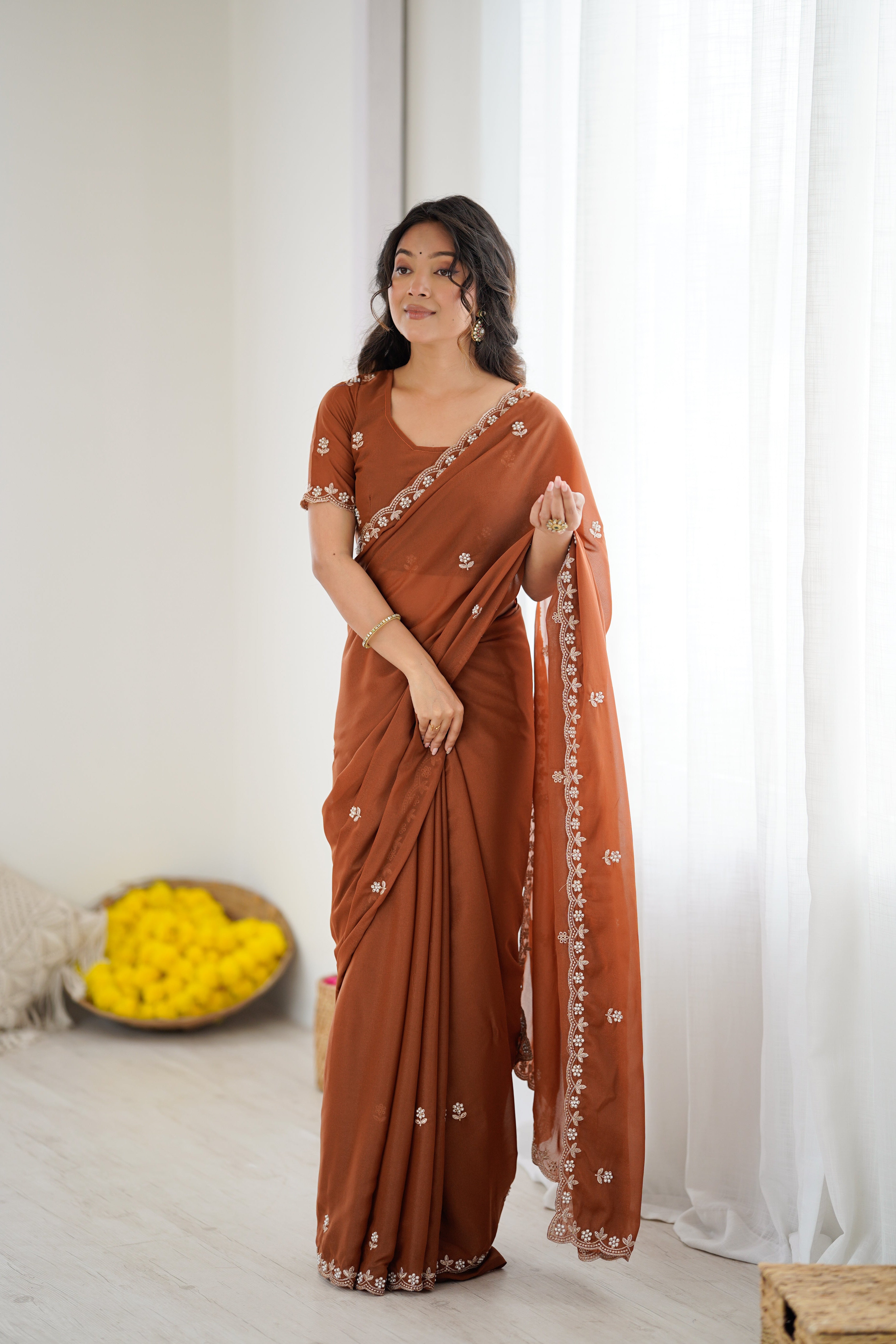 Woman wearing a brown saree with white embroidery in a minimalistic setting.