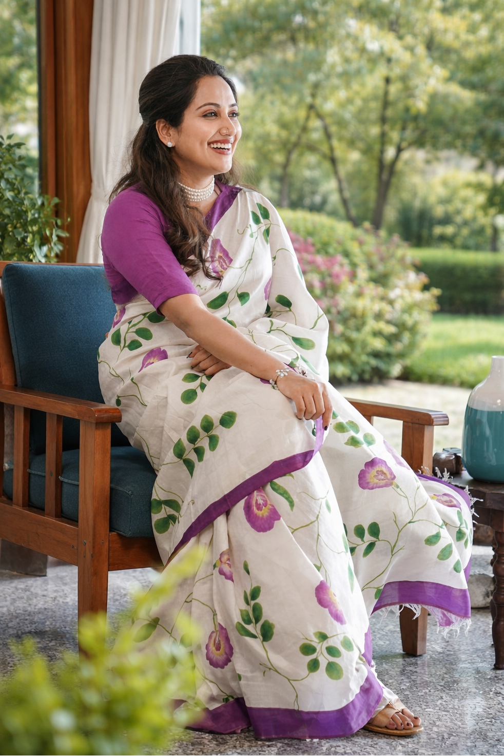 Woman in a white saree with purple accents sitting outdoors.