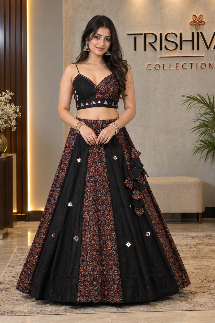 A woman models a black and rust-red printed lehenga choli outfit in a boutique setting with 'TRISHIVA COLLECTION' on the wall behind her.