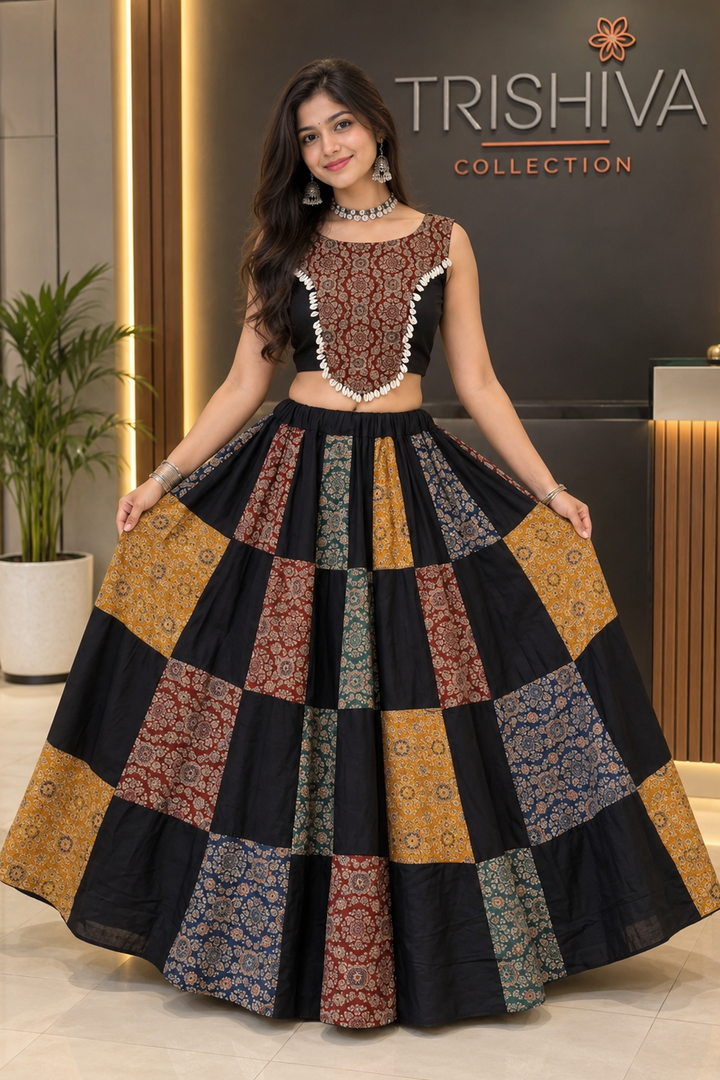 A woman modeling a Trishiva Collection ethnic outfit consisting of a black sleeveless crop top with intricate gold and red embroidery, paired with a matching flared patchwork lehenga skirt featuring multiple patterned panels in gold, red, blue, and black.
